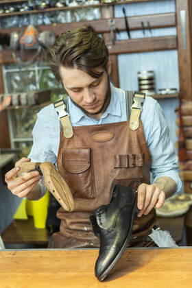 IMAGO Creative: Kreative Renaissance -- der junge Entrepreneur Male entrepreneur holding shoe stretcher while looking at shoe at workshop model released Symbolfoto property released VGF00360