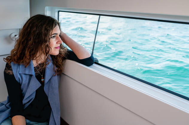 Tranquil female sitting in cabin of catamaran and looking out of window while admiring amazing view of sea on sunny day, Model released, Property released Copyright: xCarlosxPintaux MR