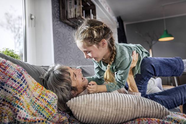 IMAGO Creative: Hygge - Winter Innendesign Grandmother playing with granddaughter while lying on sofa at home model released Symbolfoto property released AUF00617