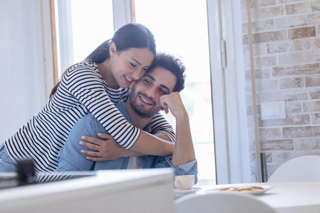 Smiling girlfriend embracing boyfriend in domestic kitchen model released Symbolfoto property released EIF01074