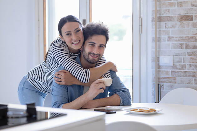 Smiling girlfriend embracing boyfriend with coffee cup in kitchen at home model released Symbolfoto property released EIF01075