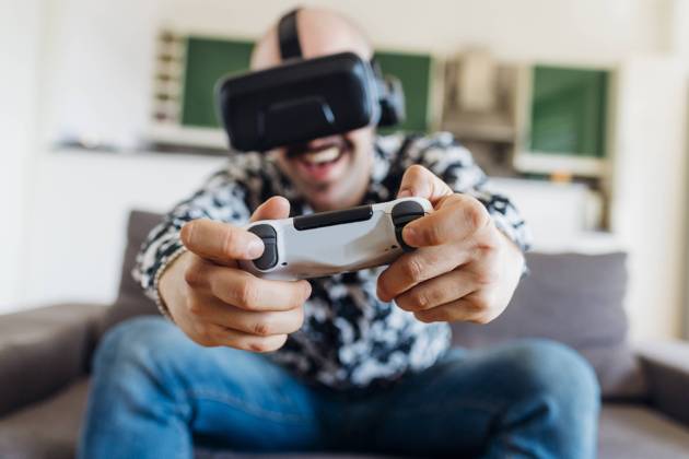 Happy man wearing virtual headset playing video game on sofa model released Symbolfoto property released MEUF03065