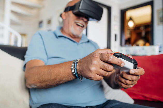 Cheerful senior man wearing virtual reality simulator playing video game at home model released Symbolfoto property released MEUF03125