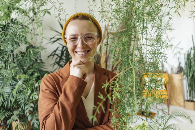 Smiling female entrepreneur with hand on chin standing by plants at work place model released Symbolfoto property released VPIF04136