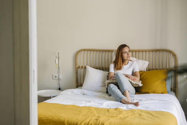 Smiling woman looking away while relaxing on bed at home model released Symbolfoto property released XLGF01844