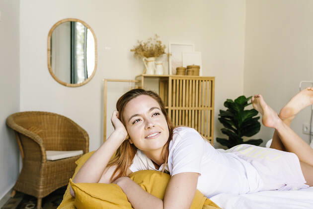 Smiling woman looking away while relaxing on bed at home model released Symbolfoto property released XLGF01893