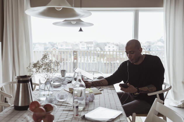 IMAGO Creative: Kreative Renaissance -- der junge Entrepreneur Hispanic male professional using mobile phone while sitting at table in living room Sweden, Gothenburg, model released, property released Copyright: xMaskotx , MA87131
