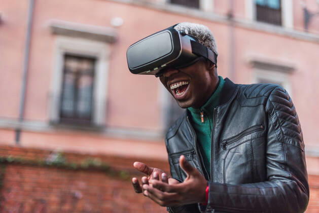Excited African American male in VR goggles experiencing virtual reality and laughing in city street, Model released Copyright: xIvanxMorenox MR