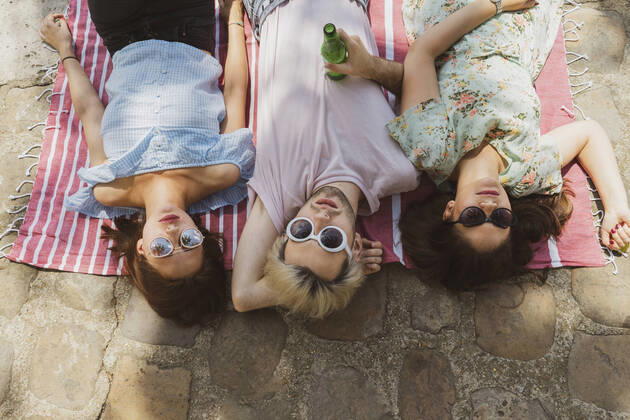 IMAGO Creative: Jahreszeit Frühling, Picknick Male and female friends relaxing on blanket during vacations model released Symbolfoto AFVF08953