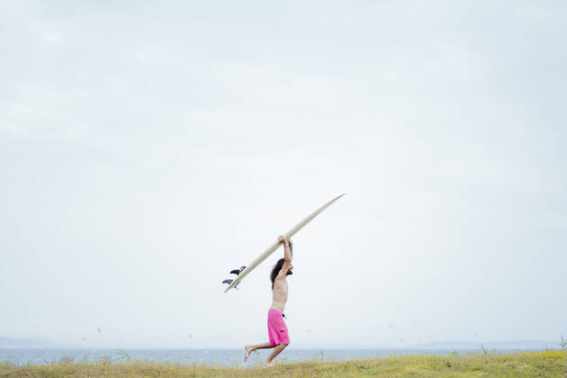 Carefree shirtless man carrying surfboard while running on meadow model released Symbolfoto property released PGF00620