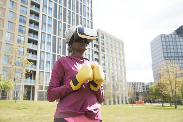 Senior woman with boxing gloves wearing virtual reality headset in park model released Symbolfoto PMF01992