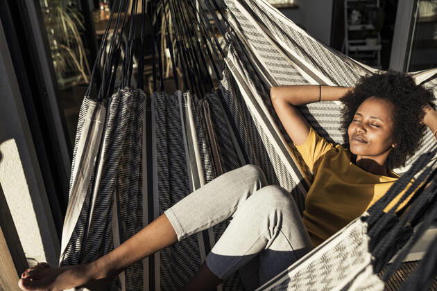 Smiling woman with hands behind head relaxing on hammock during sunny day model released Symbolfoto property released UUF23597
