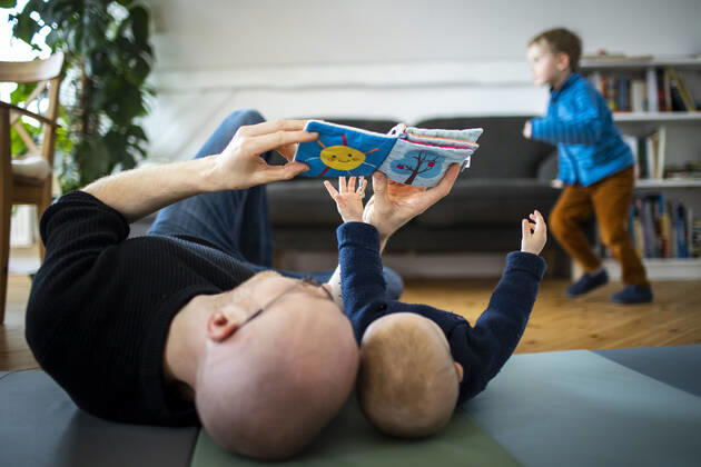 Symbolfoto: Ein Vater spielt mit seinem Baby waehrend im Hintergrund ein zweites Kind tobt. Berlin, 02.02.2021. Berlin Deutschland