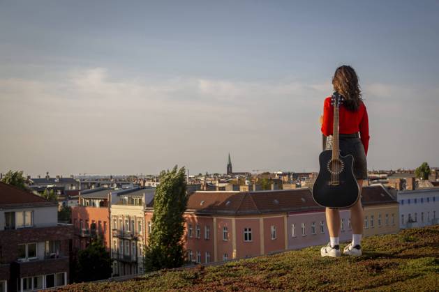 IMAGO Kreativ: Urbane Kultur - Sommer auf den Dächern Young woman carrying guitar while standing on rooftop against sky model released Symbolfoto NGF00701