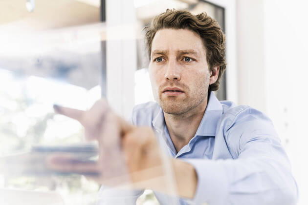 IMAGO Creative: Corporate: Klimaschutz, Digitalisierung und Urbanisierung Mid adult man pointing on glass material while sitting in office model released Symbolfoto property released UUF21891
