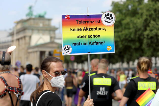 Berliner CHRISTOPHER STREET DAY 2021 - CSD - Am 24. Juli 2021 zieht der CSD in Berlin unter dem Motto SAVE OUR COMMUNITY SAVE YOUR PRIDE zum 43. Mal durch die Hauptstadt. Demoteilnehmer im Bereich des Brandenburger Tores trägt Protestschild in Regenbogenfarben mit der Aufschrift: Toleranz ist keine Akzeptanz, aber schon mal ein Anfang! PUPPLAY GERMANY - Rechts im Bild: Polizeikräfte zur Sicherung der Demonstration. Die bunte CSD-Parade startete in diesem Jahr als Demonstration an der Leipziger Straße, führte über den Potsdamer Platz, vorbei am Denkmal für die im Nationalsozialismus verfolgten Homosexuellen zum Brandenburger Tor und über die Siegessäule zur Urania. Aufgrund der Corona-Pandemie fand die Demonstration ausschließ