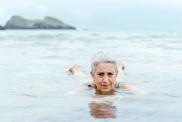 IMAGO Creative: Sommer Sport - Strand Active senior gray haired female swimming in ocean water while enjoying summertime and practicing healthy lifestyle on seashore, Model released AlbertoMenendez_OldWomanBeach_25.jpg Copyright: xAlbertoxMenendezx MR