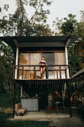 From below full body of young long haired female traveler in stylish swimwear standing on balcony of beach house located near green trees in summer day in Uvita town in Costa Rica, Model released CamilleGirard_CostaRicaTravel_73.jpg Copyright: xCamillexGirardx MR