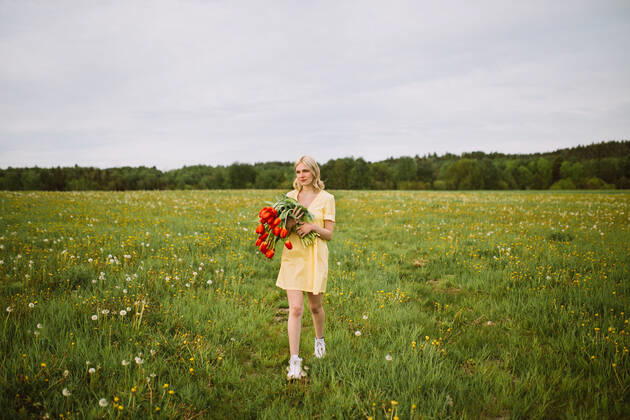 Content female in dress standing with bunch of red tulip flowers in meadow in summer and looking away CamilleGirard_GirlWithTulips_29.jpg Copyright: xCamillexGirardx Model Released