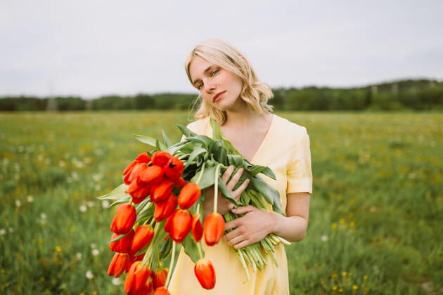 Content female in dress standing with bunch of red tulip flowers in meadow in summer and looking away CamilleGirard_GirlWithTulips_31.jpg Copyright: xCamillexGirardx Model Released