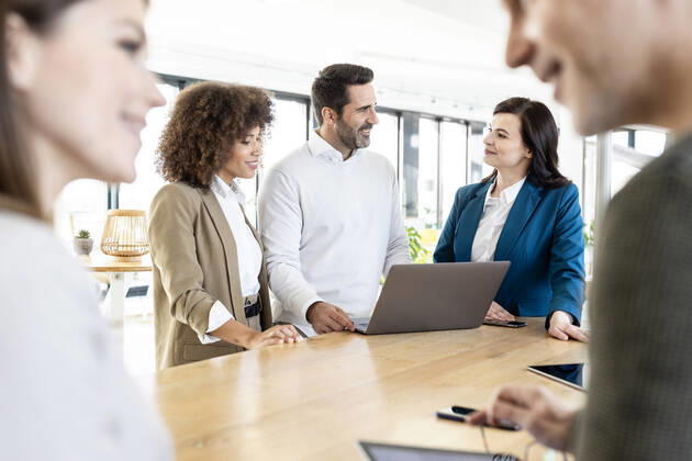 Smiling businessman planning strategy with female colleagues while standing at desk in office model released Symbolfoto property released PESF03047