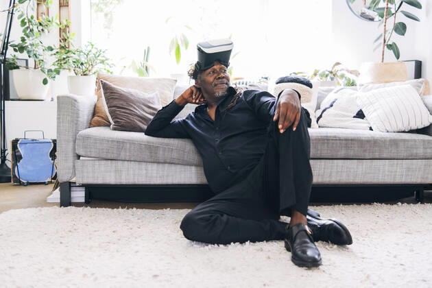 Relaxed man with virtual reality headset looking away while leaning on sofa at home model released Symbolfoto property released ASGF01083