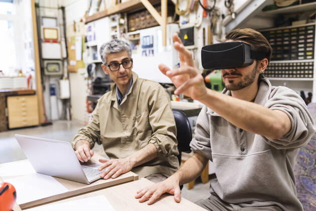 Male craftsperson using virtual reality simulator by colleague at workbench model released Symbolfoto property released MEUF03589