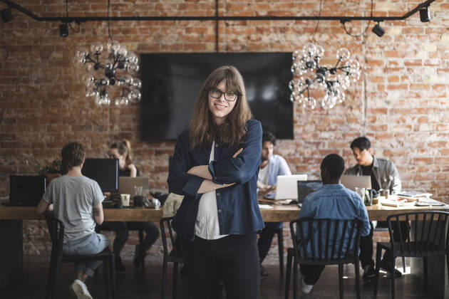 Female entrepreneur standing with arms crossed while colleagues working in creative office Sweden, Stockholm, model released, property released Copyright: xMaskotx , MA87905