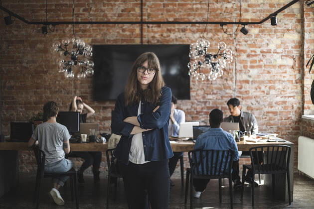 Female entrepreneur standing with arms crossed while colleagues working in creative office Sweden, Stockholm, model released, property released Copyright: xMaskotx , MA87907