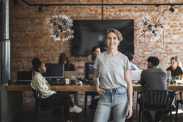Female entrepreneur standing with arms crossed while colleagues working in creative office Sweden, Stockholm, model released, property released Copyright: xMaskotx , MA87908
