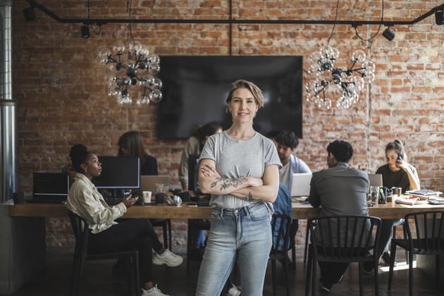 Female entrepreneur standing with arms crossed while colleagues working in creative office Sweden, Stockholm, model released, property released Copyright: xMaskotx , MA87909