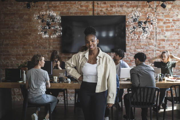 Female entrepreneur standing with arms crossed while colleagues working in creative office Sweden, Stockholm, model released, property released Copyright: xMaskotx , MA87910