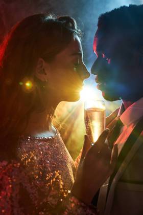 Side view of crop couple with glass on champagne in moment of kiss against shiny light ray looking at each other during party ManuelRuiz_NewYearsEvePartyCouple_31.jpg Copyright: xManuelxRuizx Model Released