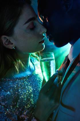 Side view of crop couple with glass on champagne in moment of kiss against shiny light ray looking at each other during party ManuelRuiz_NewYearsEvePartyCouple_34.jpg Copyright: xManuelxRuizx Model Released