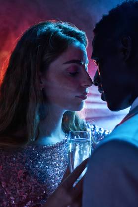 Side view of crop couple with glass on champagne in moment of kiss against shiny light ray looking at each other during party ManuelRuiz_NewYearsEvePartyCouple_36.jpg Copyright: xManuelxRuizx Model Released
