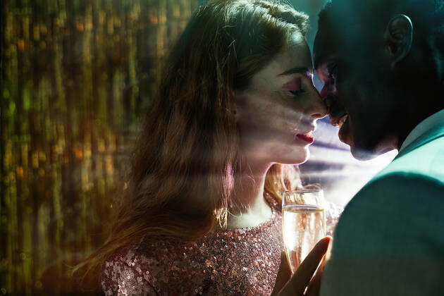 Side view of crop couple with glass on champagne in moment of kiss against shiny light ray looking at each other during party ManuelRuiz_NewYearsEvePartyCouple_37.jpg Copyright: xManuelxRuizx Model Released