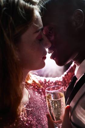 Side view of crop couple with glass on champagne in moment of kiss against shiny light ray looking at each other during party ManuelRuiz_NewYearsEvePartyCouple_38.jpg Copyright: xManuelxRuizx Model Released