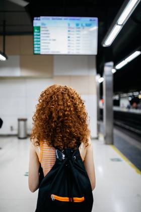 Back view of anonymous female tourist with backpack and curly hair against arrival display in underground station, Model released SergioVictorVega_AnnaTrain_11.jpg Copyright: xSergioxVictorxVegax MR