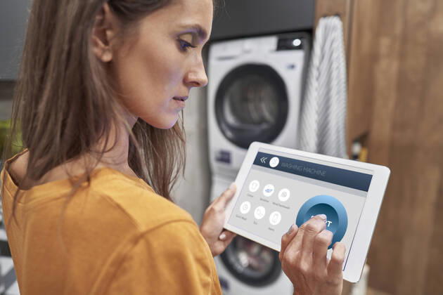 Woman using digital tablet to operate washing machine at home model released Symbolfoto property released ABIF01487