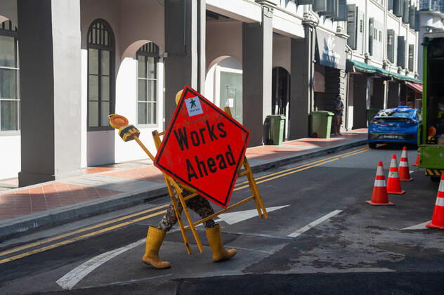 23.09.2021, Singapur, Republik Singapur, Asien - Ein Arbeiter im Stadtzentrum traegt eine Vorrichtung mit Strassenschild und Warnlicht waehrend der andauernden Corona-Krise.