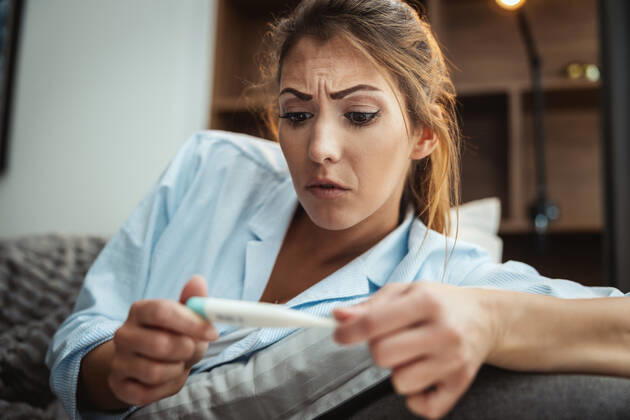 Oh No, Could It Be Flu? Young woman is lying sick at home couch and looking at thermometer. Copyright: xMilanxMarkovicx 38998936