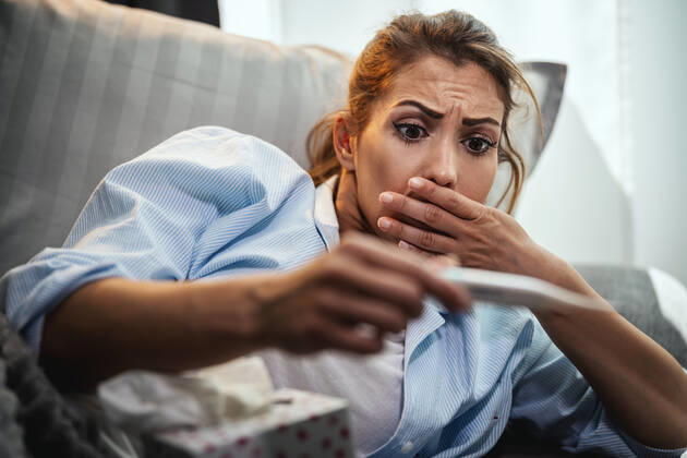 Oh No, Could It Be Flu? Young woman is lying sick at home couch and looking at thermometer. Copyright: xMilanxMarkovicx 38999806