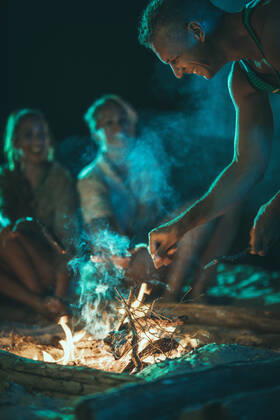 IMAGO Creative: Jahreszeit Frühling, Picknick Delicious Snacks The happy young smiling friends are sitting on the sandy seashore by the fire in the evening. They are frying sausages on stick. Copyright: xMilanxMarkovicx 39001938