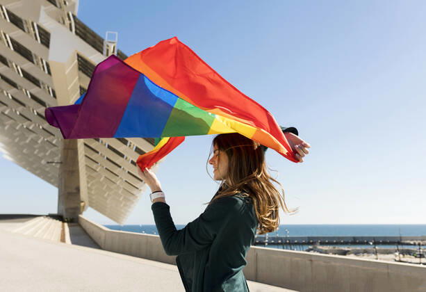 Woman holding rainbow flag near solar energy panel during sunny day model released Symbolfoto VABF04362