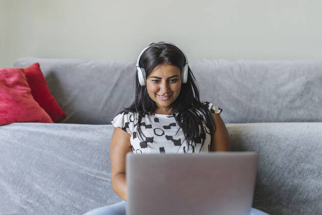 Smiling woman wearing headphones using laptop at home model released Symbolfoto property released XLGF02330