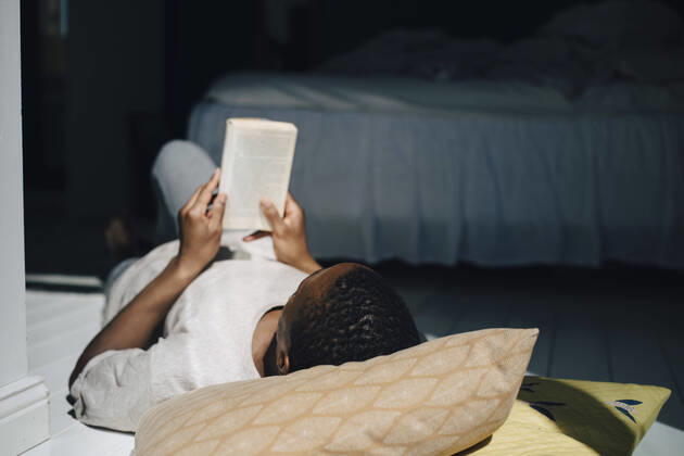 IMAGO Creative: Kulturelle Folgen der Pandemie: Gesundheitsbewußtsein und Alleinsein Man reading book while lying on floor in sunlight at home Sweden, Stockholm, model released, property released Copyright: xMaskotx , MA89989