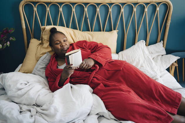 IMAGO Creative: Kulturelle Folgen der Pandemie: Gesundheitsbewußtsein und Alleinsein Creative Highlights Symbolbilder Mid adult woman reading book while relaxing on bed Sweden, Stockholm, model released, property released Copyright: xMaskotx , MA90068