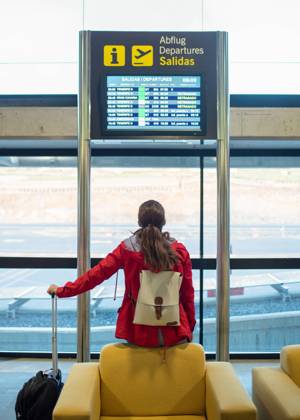 Back view of anonymous female tourist with backpack and suitcase sitting on armchair near signboard with flight schedule in airport GabrielTrujillo_La PalmaAirport_14.jpg Copyright: xGabrielxTrujillox Model Released