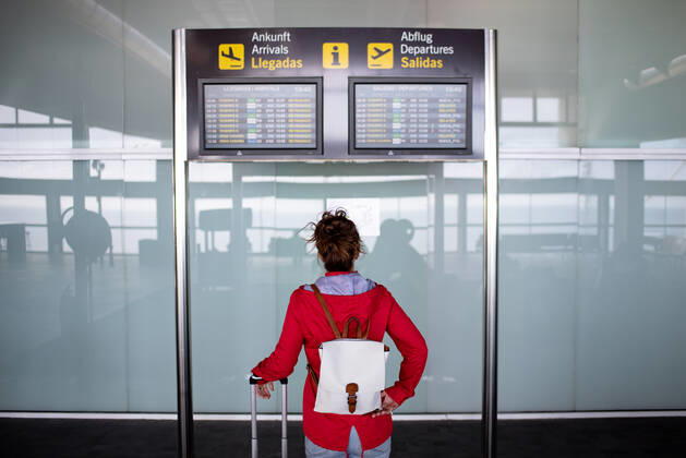 Back view of anonymous female tourist with backpack and suitcase standing near signboard with flight schedule in airport GabrielTrujillo_La PalmaAirport_33.jpg Copyright: xGabrielxTrujillox Model Released