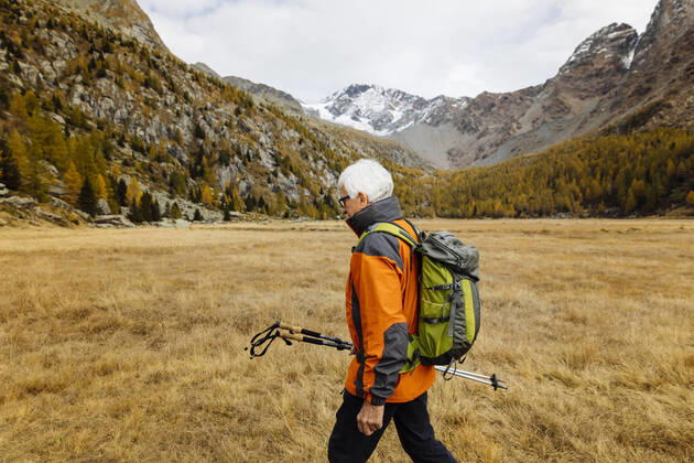 IMAGO Creative: Ende des Sommers Senior backpacker with poles hiking on grass model released, MRAF00770